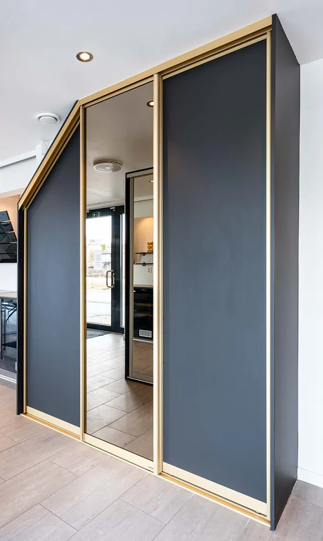 Mørkegrå skyvedører med gullramme tilpasset skråtak i moderne rom.