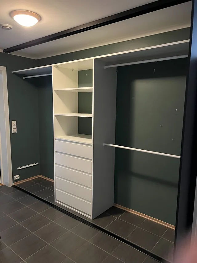 Hvit garderobe med skuffer i midten, hyller og to lange hengestenger.