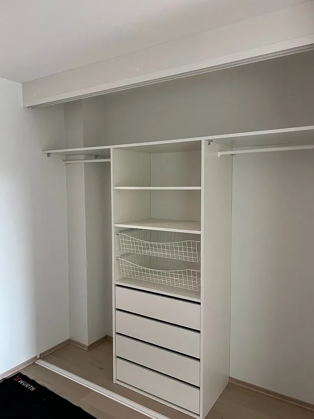 Hvit garderobe med fem skuffer, hyller, trådkurver og hengestenger.