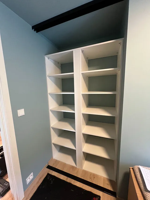 Hvit garderobe med to seksjoner fulle av åpne hyller mot grønnblå vegg.