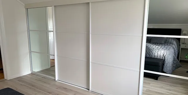 Soverom med hvit skyvedørsgarderobe, speilfelt og lyse tregulv.
