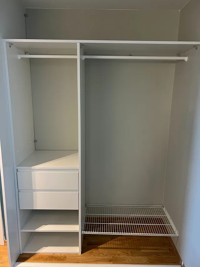 Enkel hvit garderobe med skuffer, hyller og en metallhylle nederst.