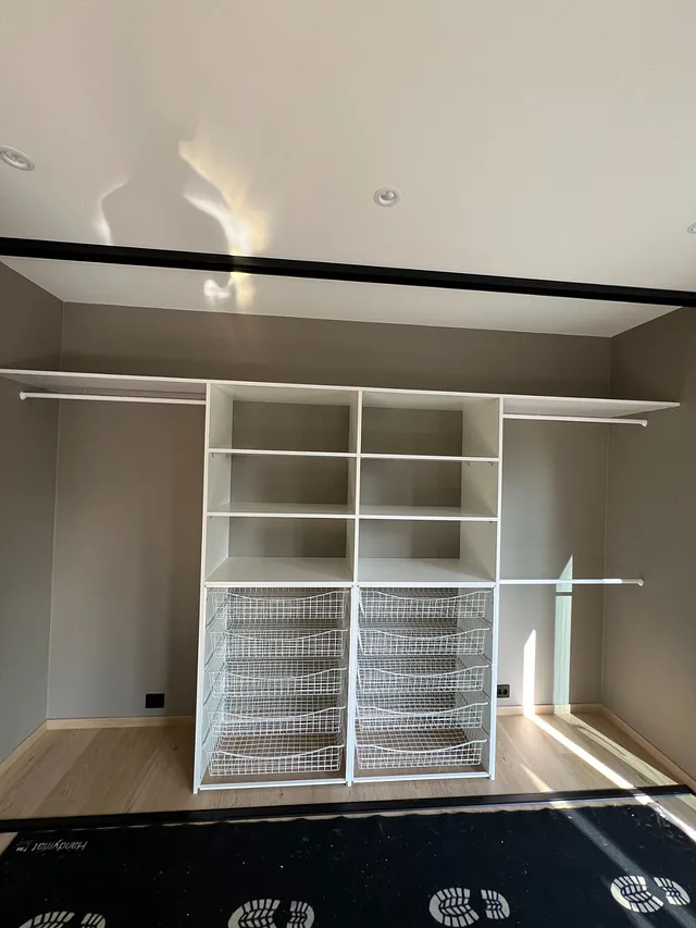 Uinnredet garderobe med hvite hyller og trådkurver under.