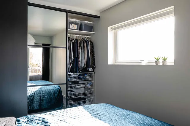 Åpen garderobe med svarte skyvedører, speilfelt og hyller med klær.